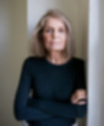 Gloria Steinem with shoulder length hair and in a long-sleeved T-shirt leans against a doorway