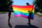 child and adult each holding one side of a rainbow flag in the sun