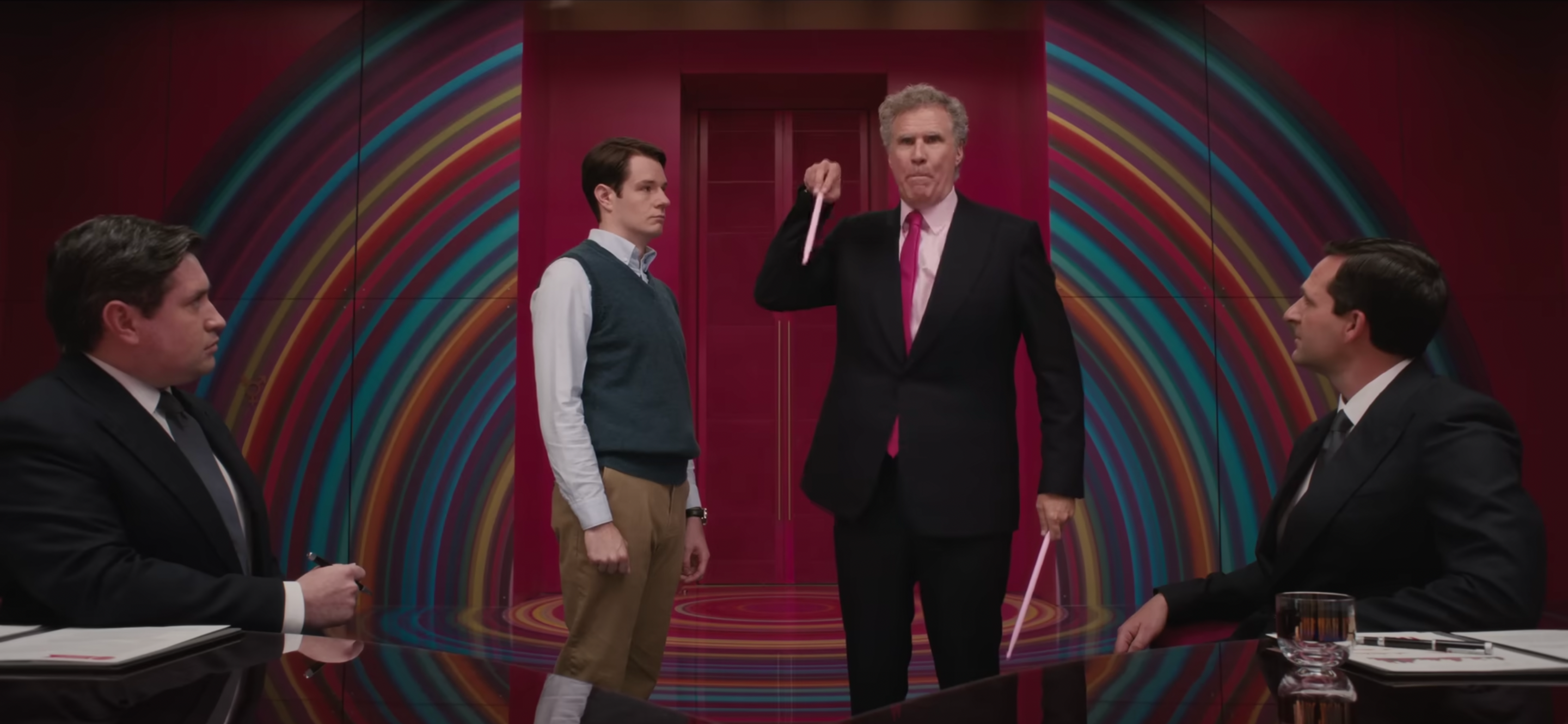In the Mattel boardroom CEO Will Ferrell holds Barbie conductor's sticks while Connor Swindells looks at him