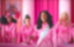 President Barbie Issa Rae with long hair and a sash is surrounded by 3 other Barbies, all in jumpsuits
