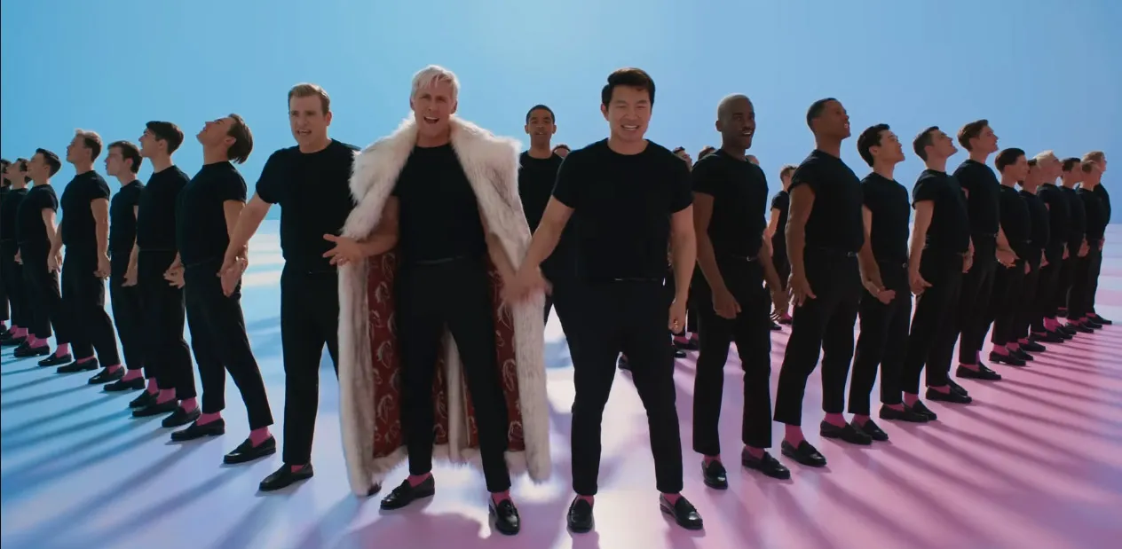 Male dancers in ankle-length trousers, loafers and T-shirts stand in formation holding hands with Ken (Ryan Gosling) in a long fake-fur coat in the middle next to Simu Liu