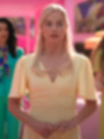 Stereotypical Barbie (Margot Robbie) with long hair parted on the side and a V-neck dress  has her hands touching and looks demure